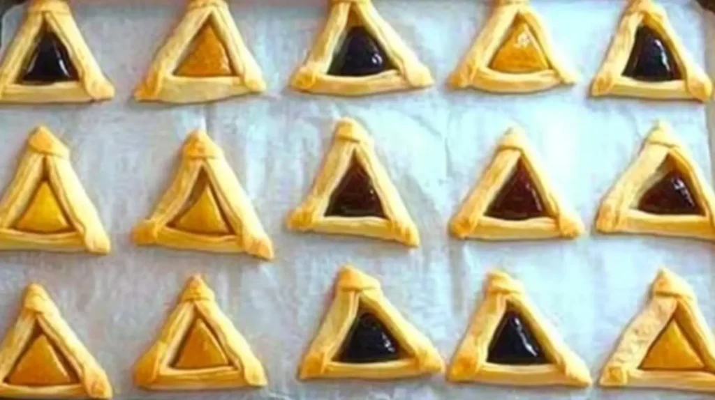 A baking sheet lightly greased, with neatly arranged hamantaschen, each evenly spaced and filled with filling, ready for baking.







